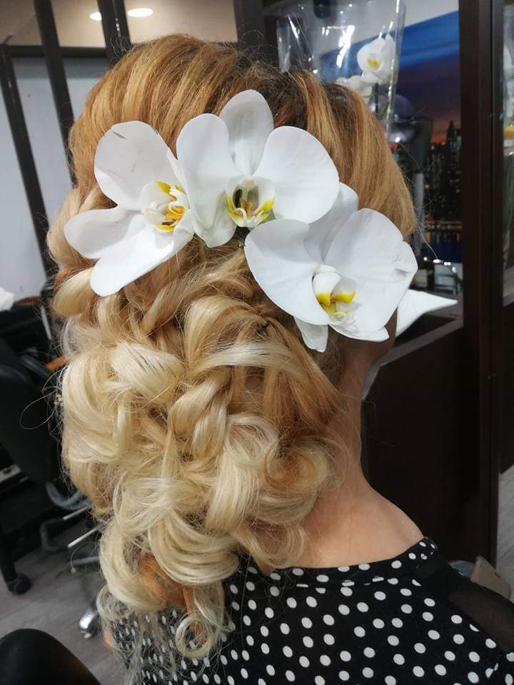 Bridal updo — romantic curled low bun on golden blonde hair adorned with white orchid flowers, back view at Divine Retreat salon