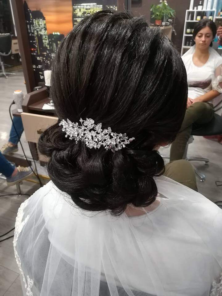 Bridal updo — elegant low curled chignon on dark brunette hair with crystal floral hairpiece and veil, back view at Divine Retreat salon