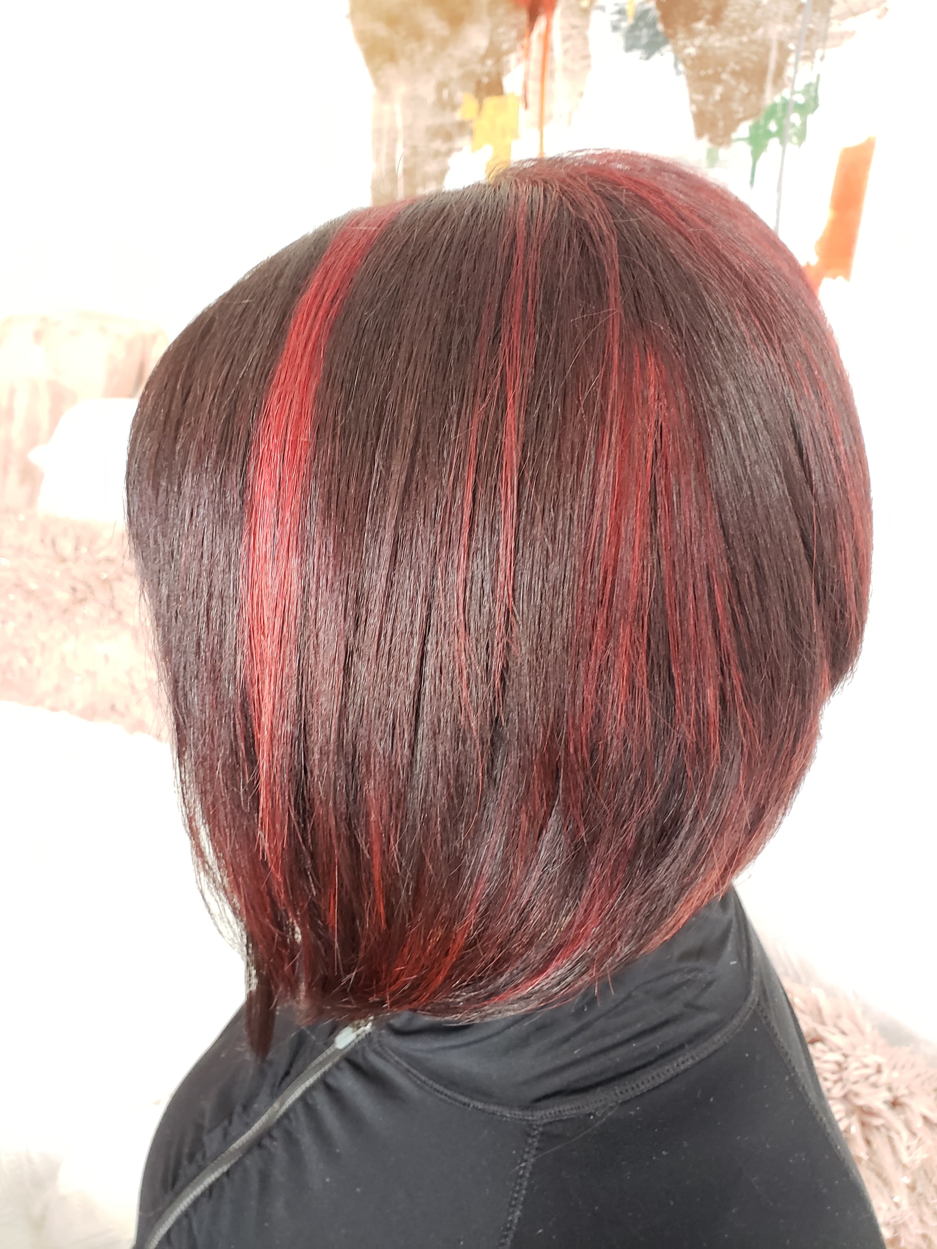 Vivid highlights — bold red peekaboo highlights through dark brunette on a short stacked bob, back view at Divine Retreat salon