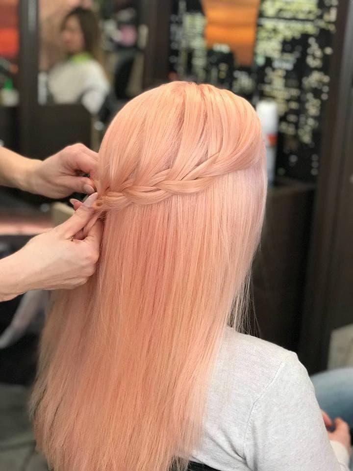 Vivid peach color with braid styling — vibrant pastel peach all-over color on long straight hair with a half-up waterfall braid being styled, back view at Divine Retreat salon
