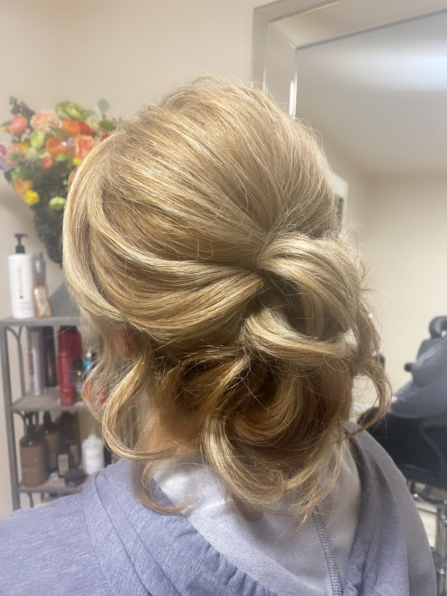 Romantic updo styling — soft textured low bun with loose curled pieces on golden blonde hair, back view at Divine Retreat salon