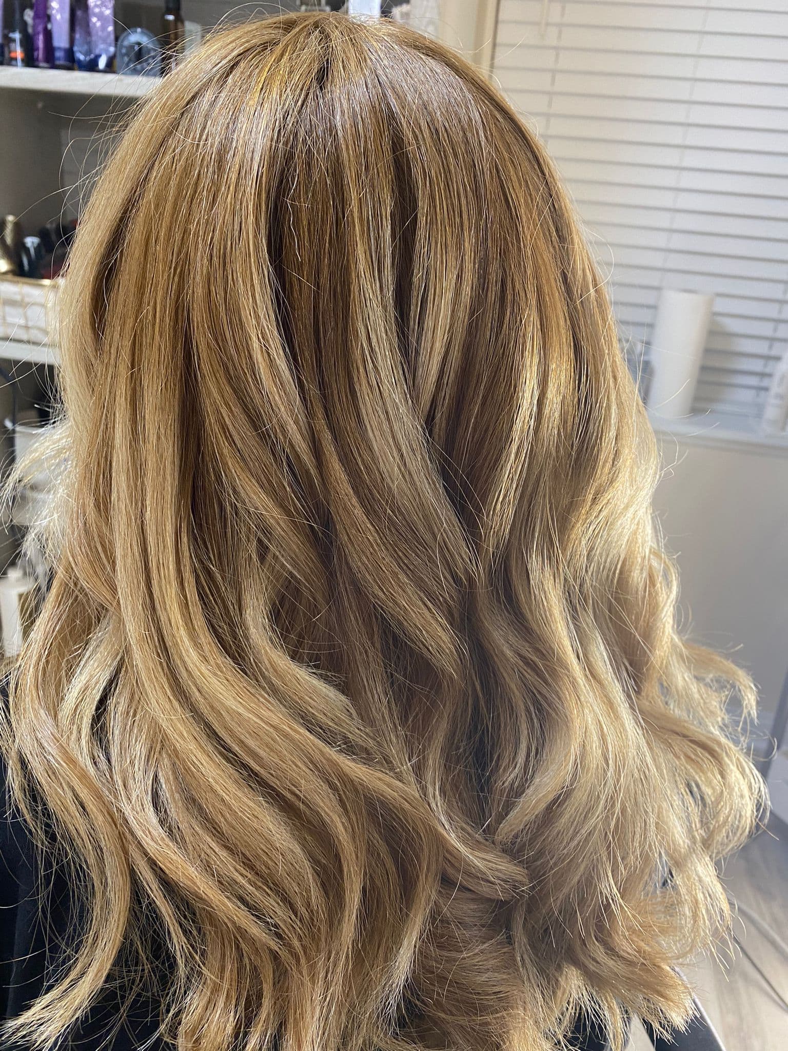 Balayage with styling — warm honey and golden blonde highlights blended into a light brunette base with soft loose waves on medium-length hair, back view at Divine Retreat salon