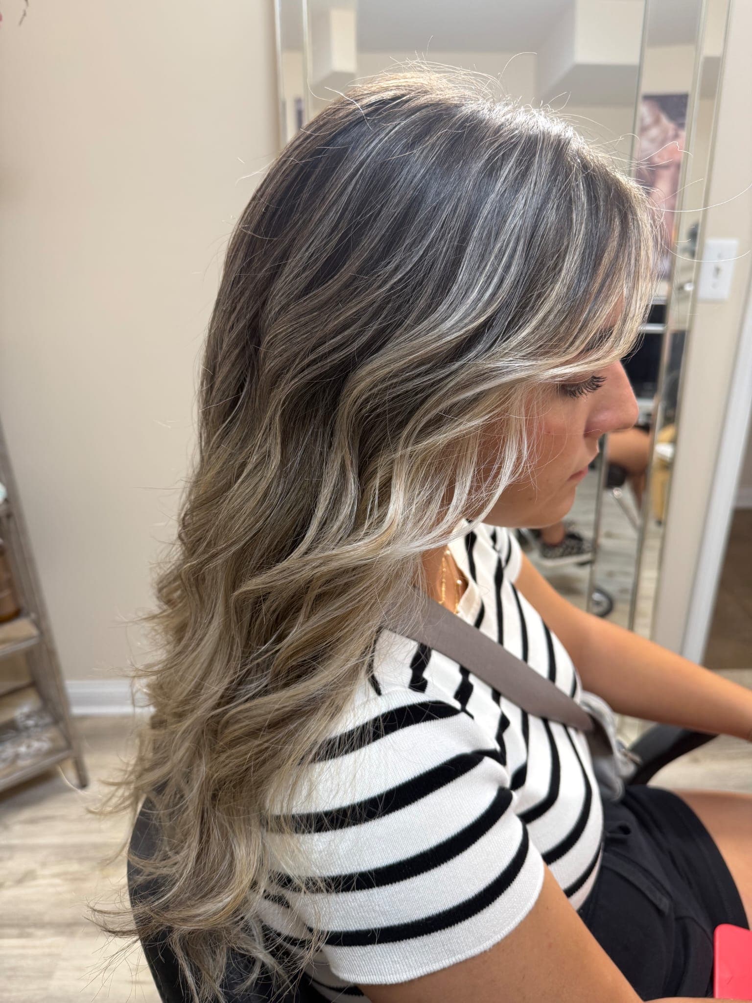 Balayage — ash blonde highlights blended into dark brunette roots with soft waves on long hair, side profile view at Divine Retreat salon