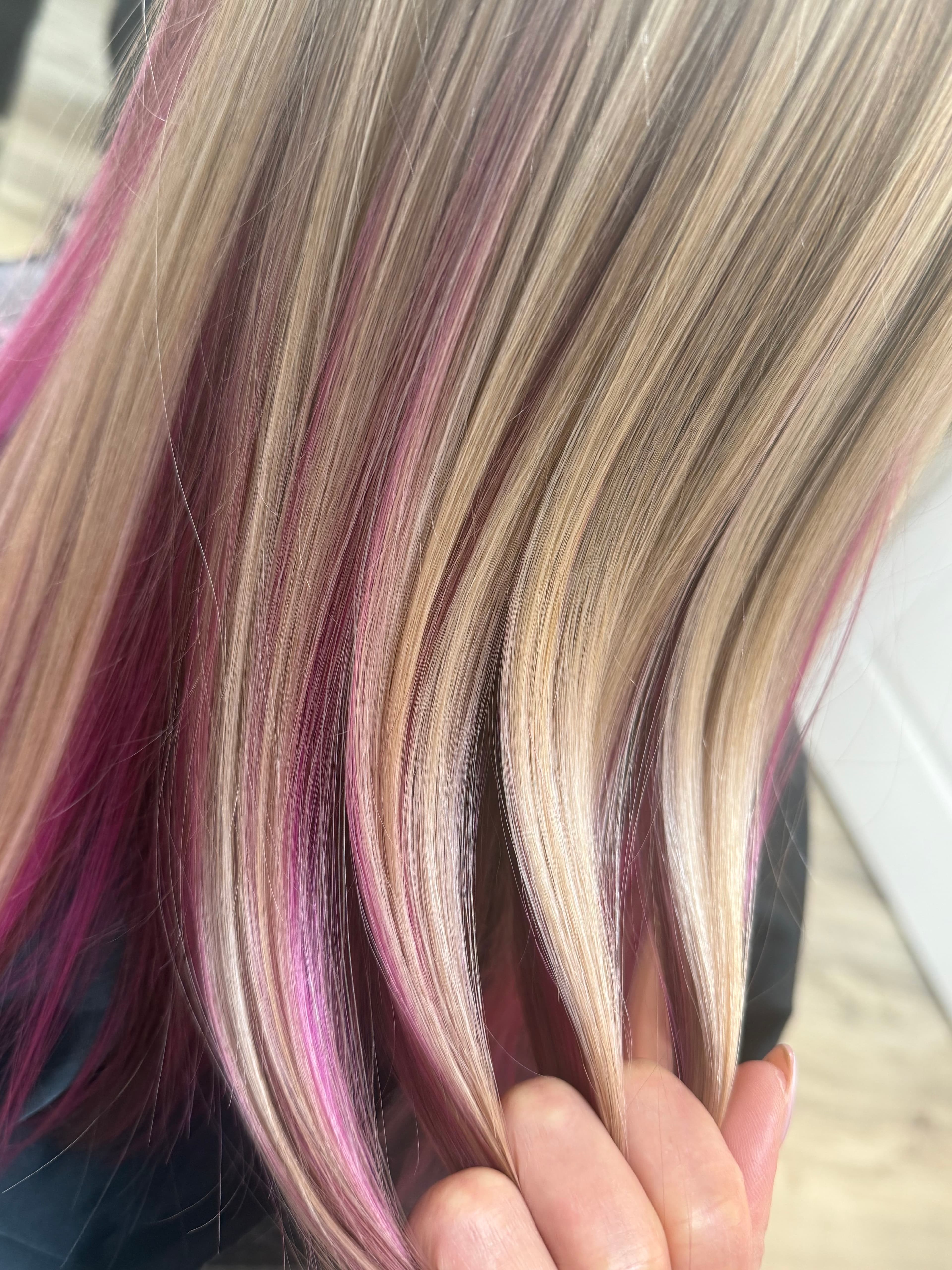 Vivid pink peekaboo color — bold magenta-pink accent panels woven through sandy blonde and platinum highlights on long straight hair, close-up detail view at Divine Retreat salon